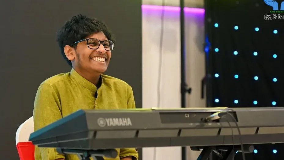 A young man smiling as he plays the keyboard on stage.